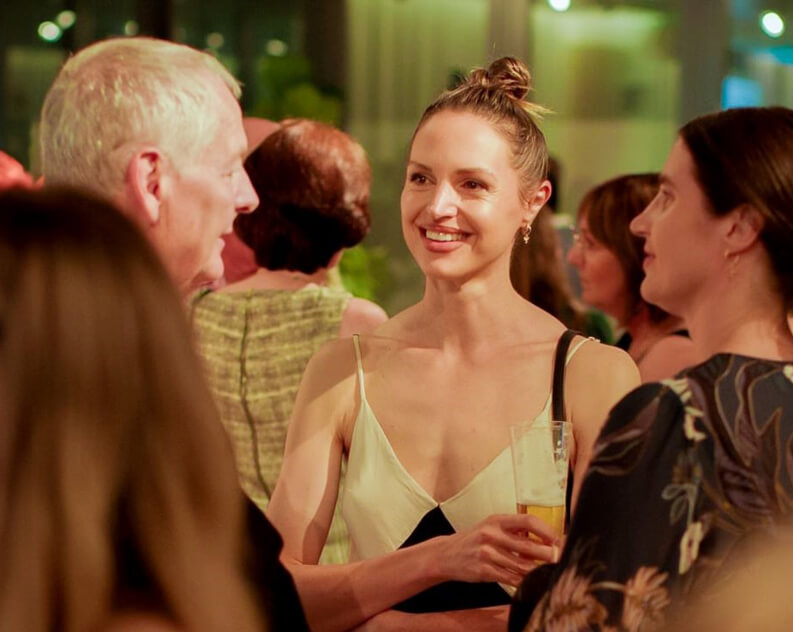 Smiling women and a man in conversation at a social gathering, with a woman holding a glass of drink.