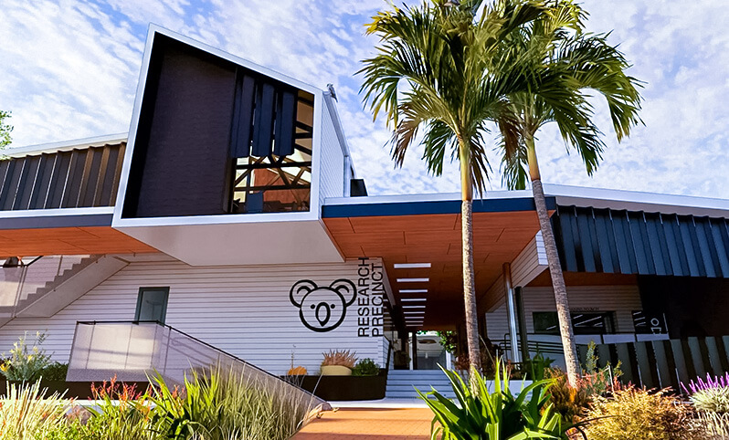 A modern research building with sleek architecture, large windows, and a landscaped area with palm trees. The structure prominently displays the words