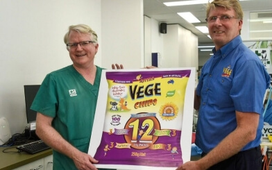 Smiling man in a teal shirt holds a large bag of Vege chips promotional poster.