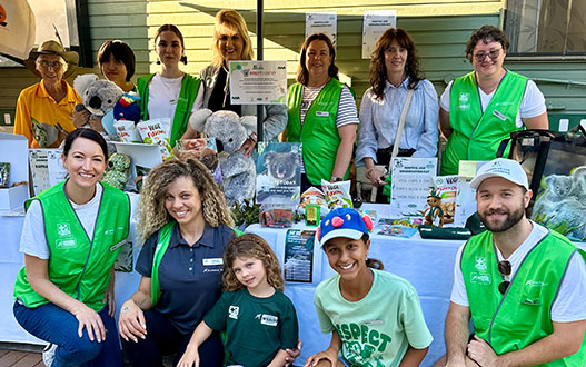 A group of people wearing green vests pose behind a table with animal-themed items and informational materials, likely at an event or fundraiser.