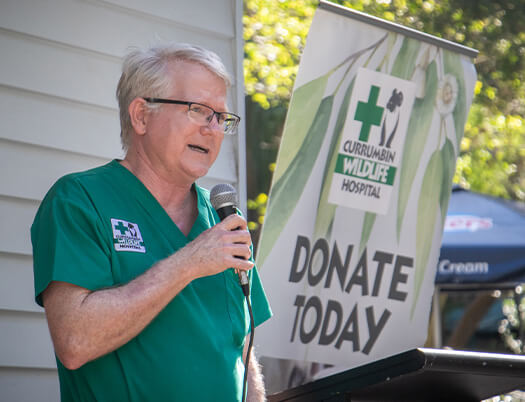 A person in green scrubs speaks into a microphone next to a Currumbin Wildlife Hospital “Donate Today” sign.