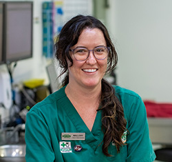 Smiling female wildlife vet in green scrubs in front of monitors in a medical setting