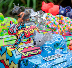 Colorful, decorated koala sculptures are displayed outdoors, each uniquely painted with bright patterns and designs.