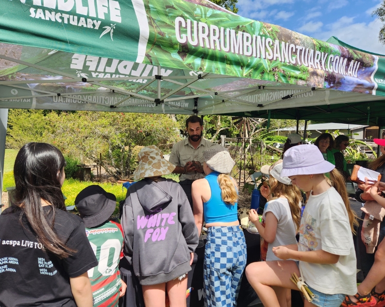 A large group of kids gather around a stall with a man in khaki standing behind it