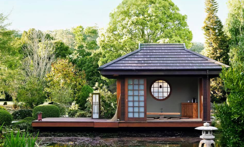 Traditional wooden open Japanese teahouse set on a lake surrounded by large green trees and bushes
