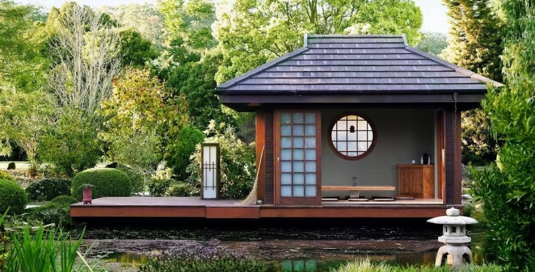 Japanese wooden teahouse on a platform on a lake, surrounded by greenery
