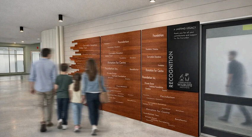 Family walking by a recognition wall displaying donor names.